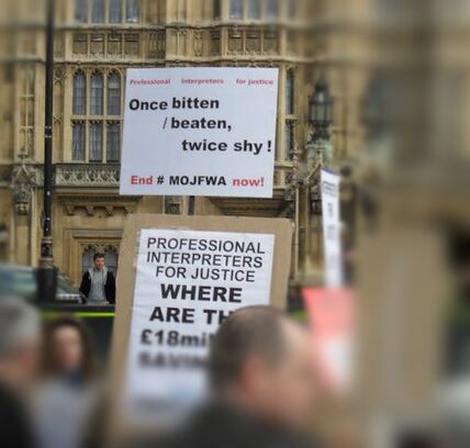 Photograph of public service interpreters demonstrating in front of Houses of Parliament with placards: Professional Interpreters for Justice, Once bitten / beaten, twice shy! End #MOJFWA now! Professional Interpreters for Justice Where are the £18 million savings! #MOJFWA